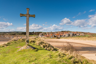 View of Alnmouth across the sand dunes, with a large wooden cross in the foreground